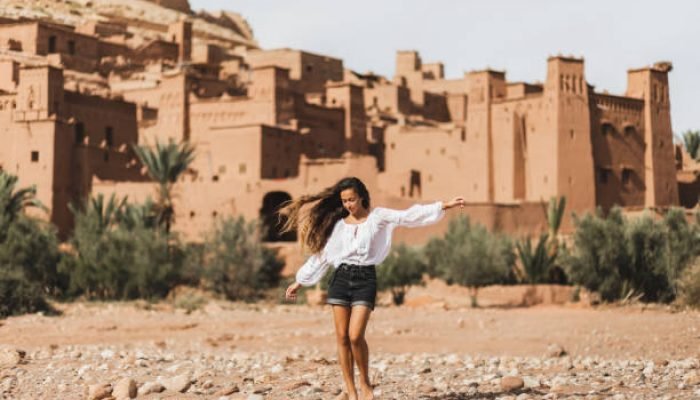 Young curly woman eastern appearance walking on background of kasbah Ait-Ben-Haddou. Travel in Morocco, Ouarzazate. Summer vacations, travel lifestyle concept.